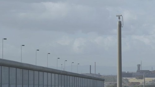 Distant photo of prison wall and security camera on a pole